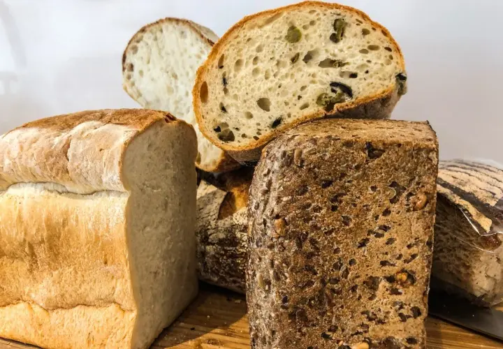 Różnorodne pieczywo, w tym bochenek z ziarnami i kromka z oliwkami. Czy chleb żytni ma gluten? Tak, większość chlebów, w tym żytni, zawiera gluten.