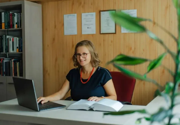 Uśmiechnięta prawniczka przy biurku z laptopem i książką. Dowiedz się, ile kosztuje sprawa o zasiedzenie u adwokata.