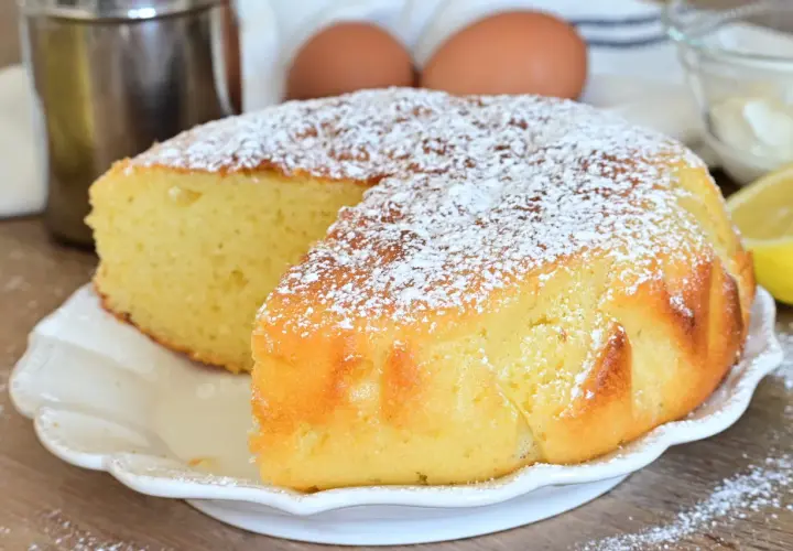 Una soffice torta al limone, spolverata di zucchero a velo, pronta per essere gustata. Ingredienti freschi come uova e limone sullo sfondo.