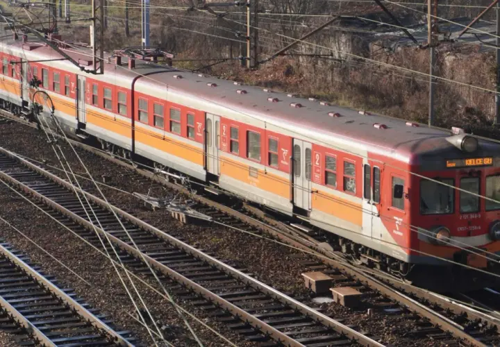 Czerwono-pomarańczowy pociąg elektryczny EN57 na torach.