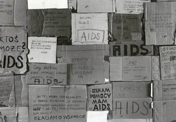 Ludzie błagają o pomoc, umierają na AIDS. Kartony z napisami "SOS", "Help", "Proszę o pomoc" świadczą o desperacji i walce o życie w obliczu choroby, która w tamtych czasach była naznaczona stygmatyzacją i brakiem wsparcia, tworząc swoistą **hegemonię*...