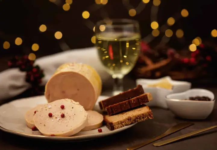 Tranche de vin foie gras sur une assiette, avec du pain d'épices et un verre de vin blanc. Ambiance festive.