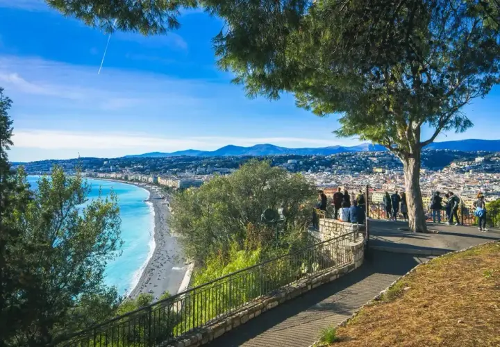 Widok na lazurowe morze i Niceę, stare miasto z promenadą. Ludzie podziwiają panoramę z tarasu widokowego.