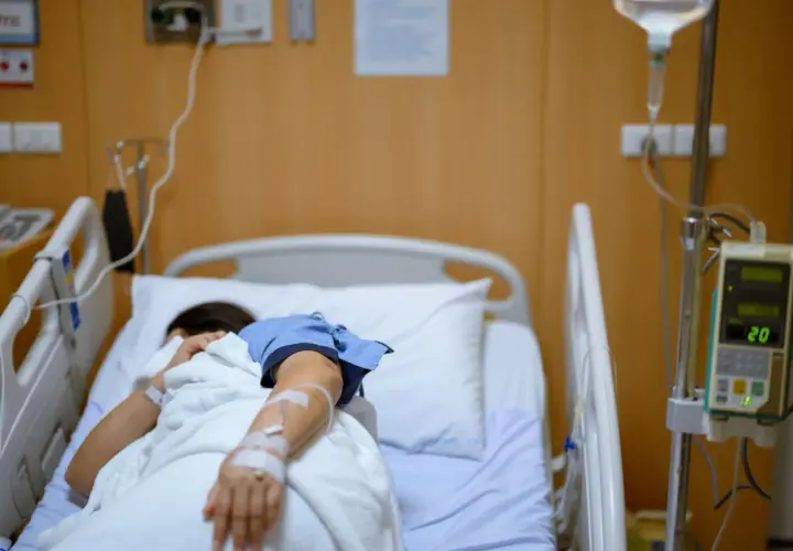 Pacjentka w szpitalnym łóżku, podłączona do kroplówki, walczy z chorobą, która przypomina dżumę.