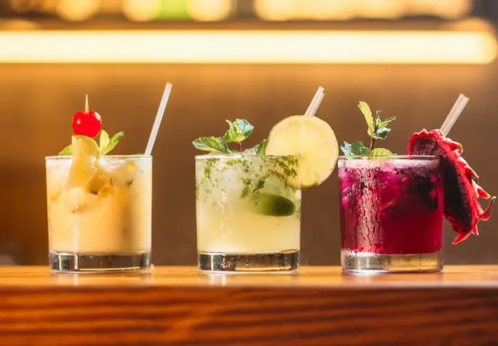 Trzy kolorowe drinki na barze: żółty z wiśnią, zielony z limonką i miętą, oraz fioletowy z pitają. Idealne do letnich wieczorów, a może i z **kazbek peak brandy z czym pić**?