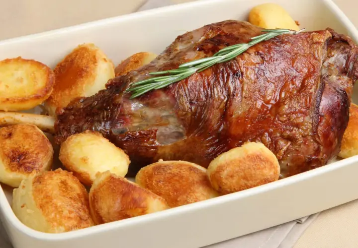 Gigot d'agneau rôti, garni de romarin, entouré de pommes de terre au four dorées et croustillantes. Un plat savoureux prêt à être dégusté.