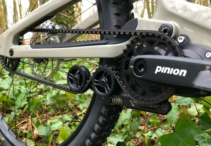 Close-up of a belt drive mountain bike's drivetrain, featuring a Pinion gearbox and Gates Carbon Drive belt, ready for off-road adventures.