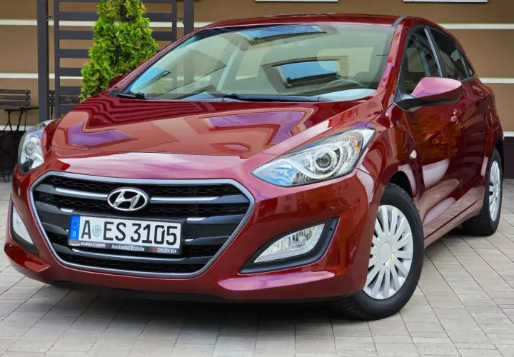 Czerwony Hyundai i30 1.6 CRDi lśni w słońcu, zaparkowany na kostce brukowej przed domem.