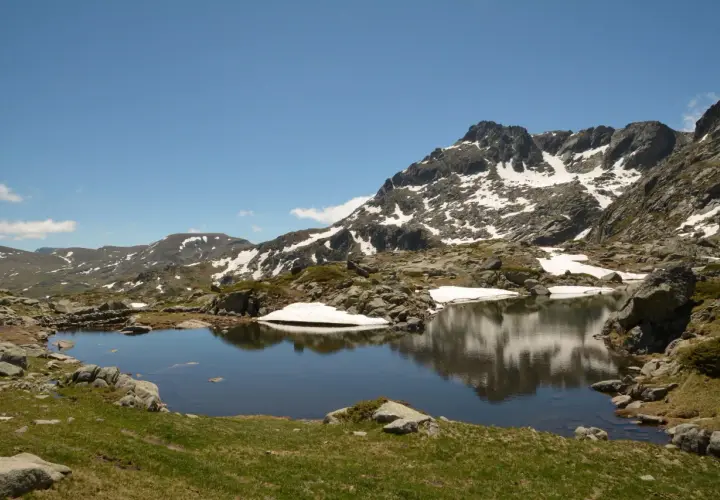 Góry Pirin z jeziorem odbijającym skaliste szczyty i resztki śniegu.