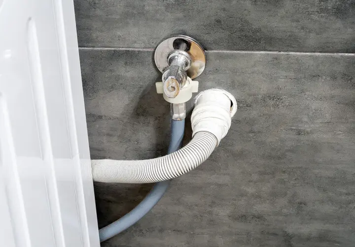 Instalacja odpływu do pralki. Wąż odpływowy podłączony do syfonu pod zlewem, na odpowiedniej wysokości.