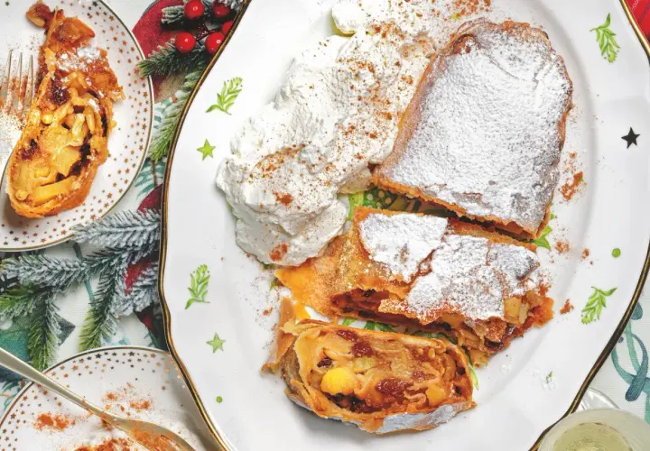 Delizioso strudel di mele con pasta sfoglia, cosparso di zucchero a velo e servito con panna montata e cannella.