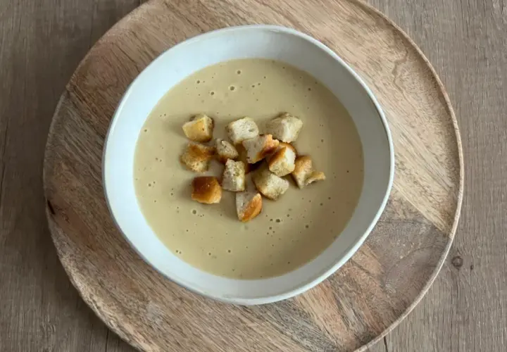 Aksamitna zupa cebulowa krem, udekorowana chrupiącymi grzankami, podana na drewnianej desce.