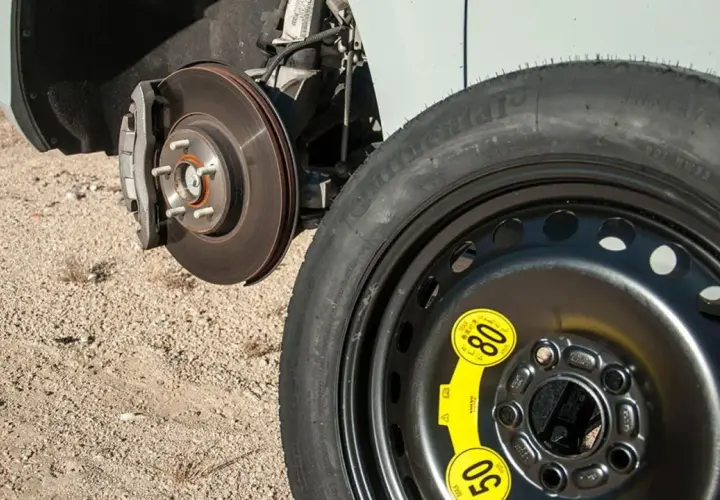 Rueda de galleta de repuesto junto al disco de freno de un coche, lista para ser instalada.