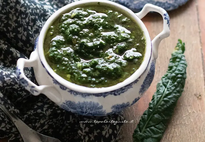 Pesto di cavolo nero in una ciotola decorata, accanto a una foglia fresca. Un condimento sano e saporito.