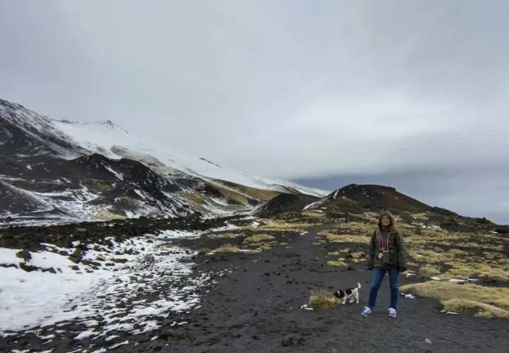 Una donna e il suo cane esplorano il paesaggio lunare dell'Etna in Sicilia, con neve e rocce vulcaniche.