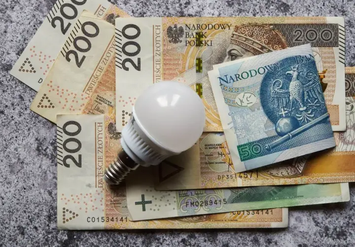 Żarówka LED na stosie banknotów 200 zł i 50 zł. Zastanawiasz się, ile za prąd miesięcznie zapłacisz?