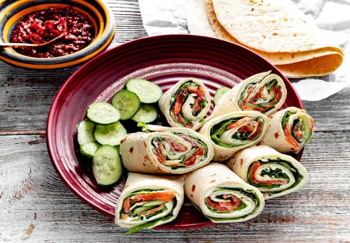 Roladki z tortilli z łososiem, świeżym ogórkiem i sałatą, podane z pikantnym sosem.