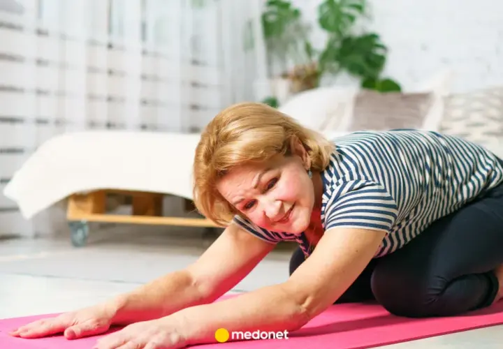 Starsza kobieta wykonuje ćwiczenia na osteoporozę na różowej macie w domu.