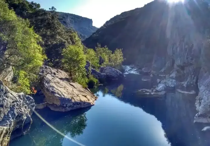 El río fluye sereno en la Foz de Lumbier, rodeado de imponentes rocas y vegetación exuberante bajo un sol radiante.