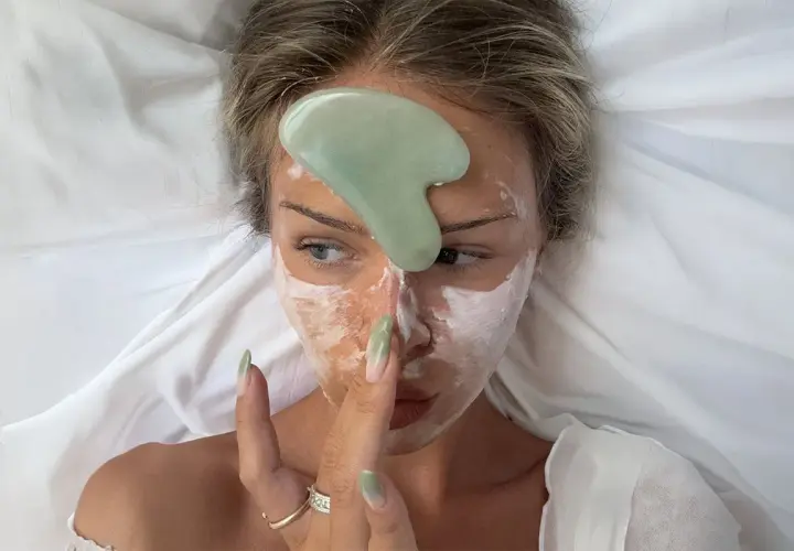 En kvinna med ansiktsmask och en grön gua sha-sten på pannan.