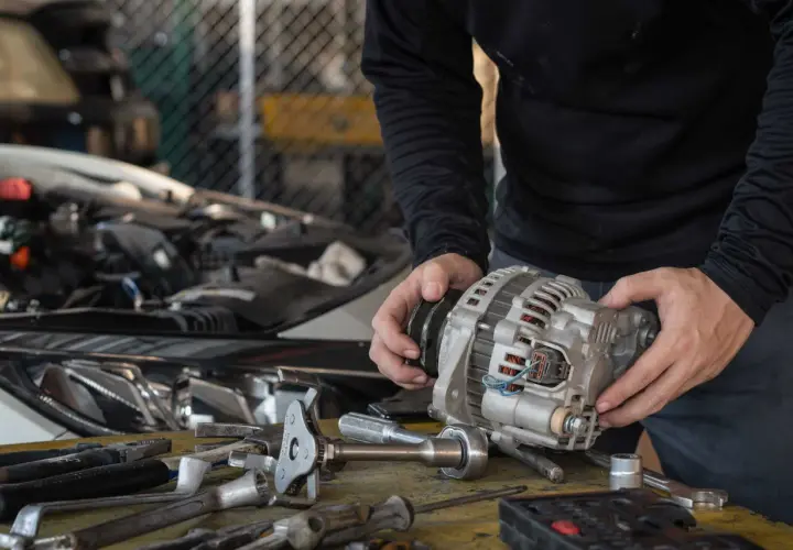 Mechanik trzyma alternator, zastanawiając się, ile trwa regeneracja alternatora. Na stole leżą narzędzia.