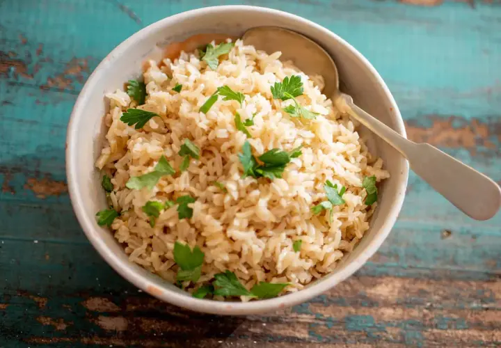Un tazón de arroz integral cocido con perejil fresco y una cuchara.