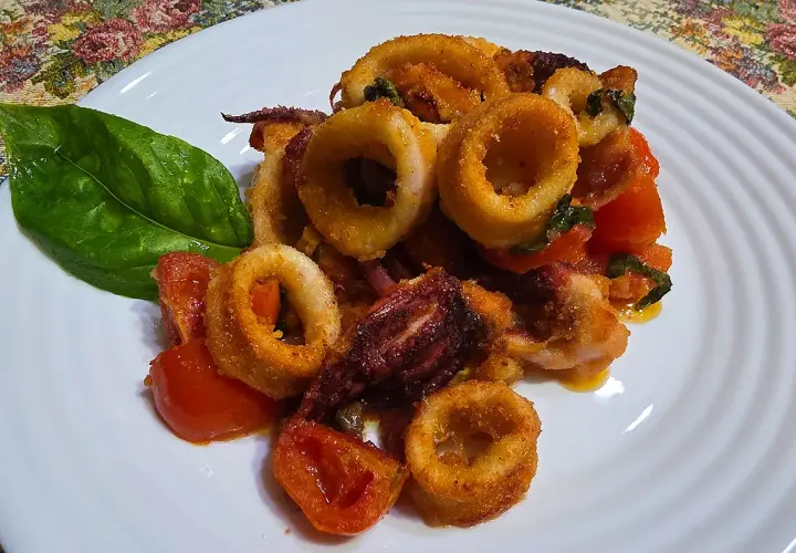 Anelli di calamari croccanti e pomodorini cotti nella friggitrice ad aria, guarniti con una foglia di basilico.