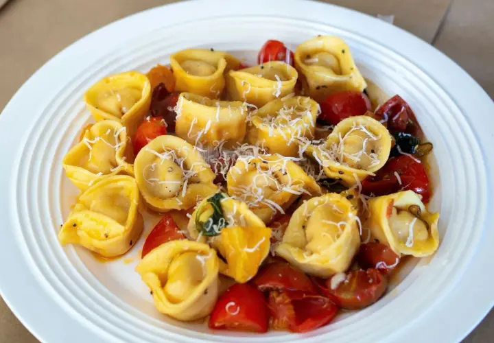 Domowe tortellini z mięsem, pomidorkami i parmezanem na białym talerzu.