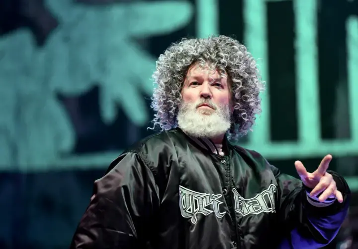 Fred Durst z Limp Bizkit na koncercie, z charakterystyczną fryzurą i brodą, w czarnej kurtce z logo zespołu.