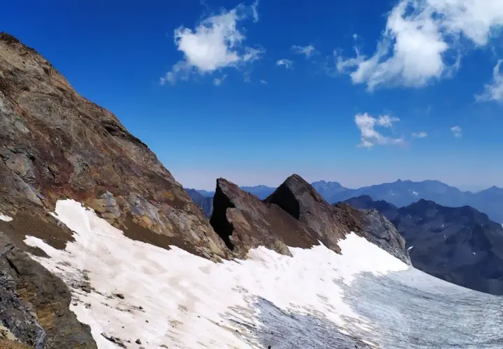Paisaje de alta montaña con nieve y rocas en el pico Viñamala. El cielo azul intenso contrasta con las cumbres nevadas y las formaciones rocosas.