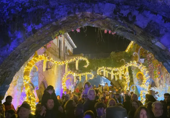 Gente disfrutando del mercado navideño en Cartes, con luces brillantes y ambiente festivo bajo un arco de piedra.