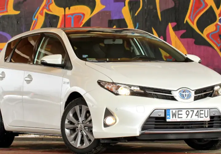 Biała Toyota Auris 2015 z polskimi tablicami rejestracyjnymi WE 974EU zaparkowana przed kolorowym muralem.