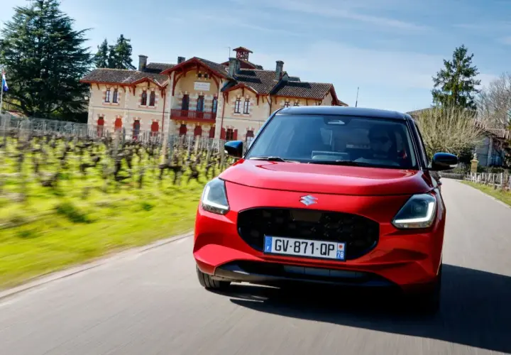 Czerwony Suzuki Swift pędzi drogą obok winnicy i zabytkowego domu.