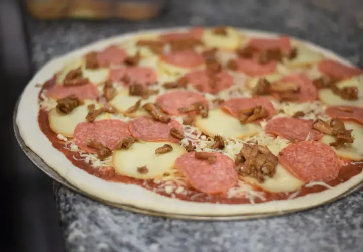 Gotowa do pieczenia pizza z salami, mozzarellą i grzybami. Idealna na kolację po włosku.