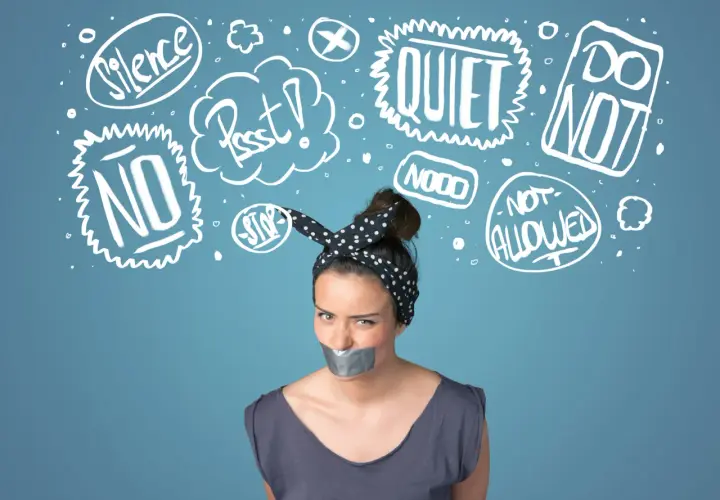 Kobieta z zaklejoną taśmą ustami, otoczona chmurkami z napisami "Silence", "Quiet", "No", "Stop", symbolizującymi tłumienie emocji.