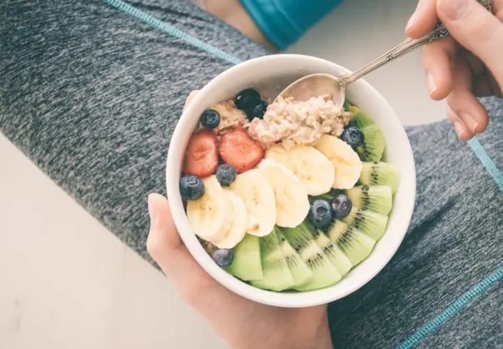 Miseczka owsianki z owocami: truskawkami, bananem, kiwi i borówkami. Idealne jedzenie po treningu.