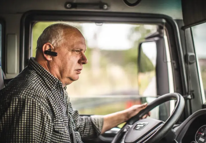 Kierowca ciężarówki w słuchawce Bluetooth, skupiony na drodze. Przestrzega rozporządzenie 561 czas pracy kierowców, dbając o bezpieczeństwo.