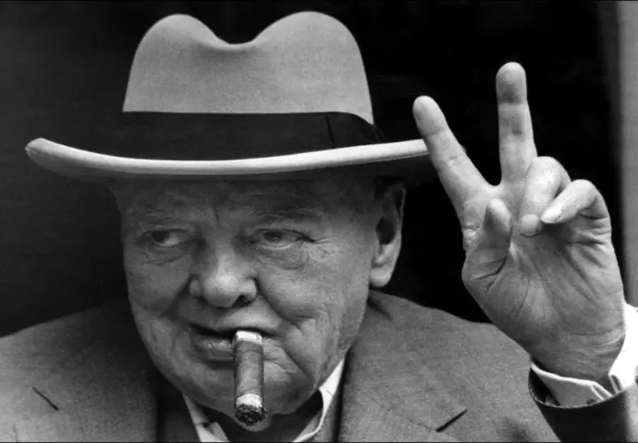Winston Churchill, chapeau, cigare et signe de victoire. L'alcool et le cigare font partie de son image iconique.
