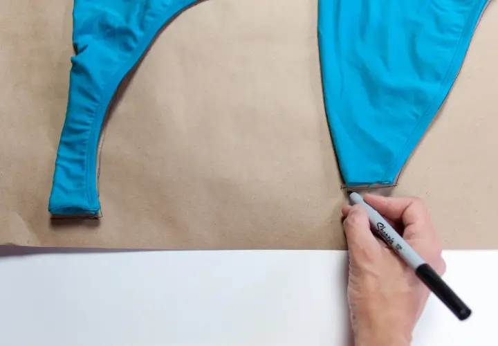 Tracing a blue swimsuit piece onto brown paper, a step in how to make a swimsuit.