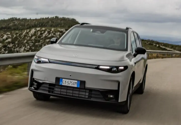 Leapmotor C10 REEV in grigio chiaro sfreccia su una strada panoramica, con un guidatore al volante.