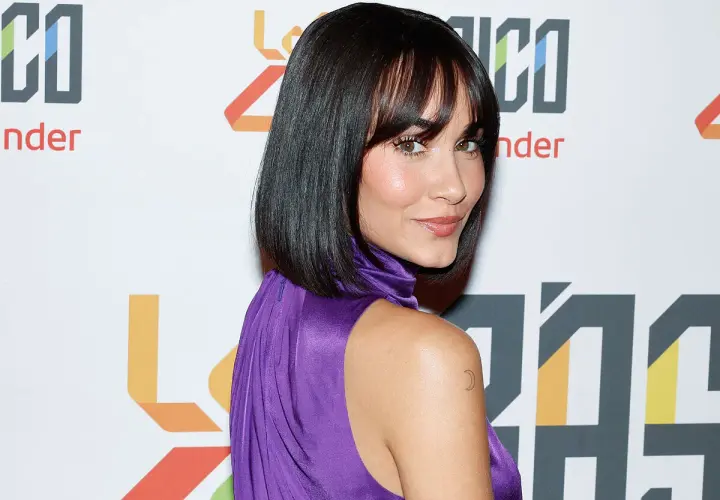 Mujer con un elegante flequillo para frente grande, cabello oscuro y vestido morado. Luce un tatuaje de luna en el hombro.