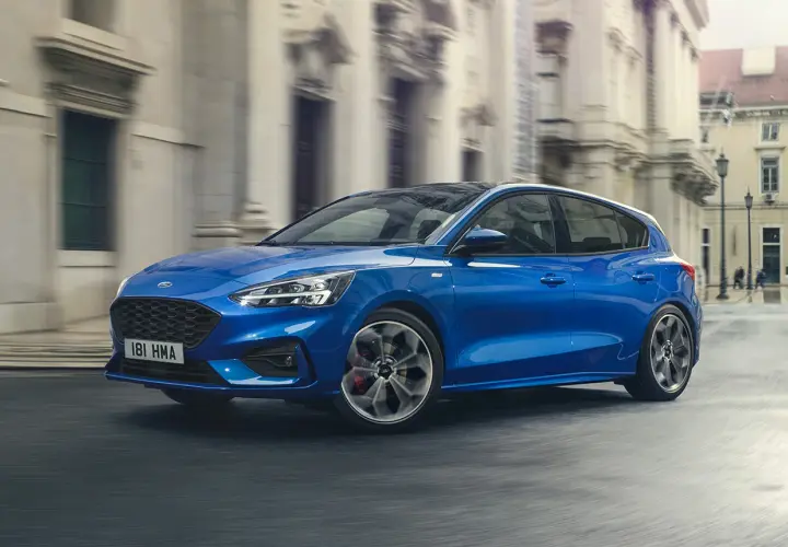 Ford Focus blu in movimento, disponibile con motori a benzina e diesel, sfreccia in una strada cittadina.