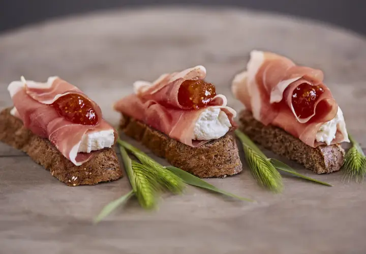Drei kleine Brote mit Frischkäse, Feigenmarmelade und Schinken – so sieht ein köstliches Crudo aus.