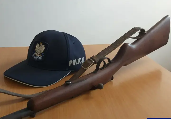 Policyjna czapka i karabin, prawdopodobnie kbks bez pozwolenia, leżą na drewnianym stole.