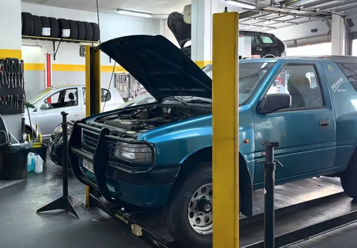 Taller mecánico con coches, neumáticos y herramientas. Se ven las copelas de un coche azul, parte del motor y la carrocería.