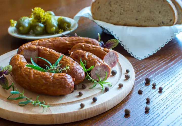 Pyszna kiełbasa z piekarnika, podana z chlebem i ogórkami, ozdobiona rozmarynem i pieprzem.