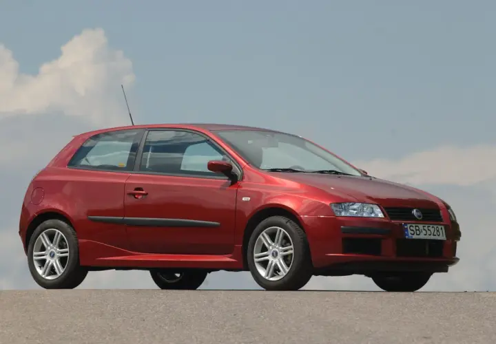 Czerwony Fiat Stilo 1.9 JTD z felgami aluminiowymi stoi na tle błękitnego nieba z chmurami.