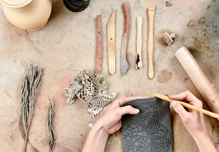 Mani che lavorano con il das adulti, creando un motivo a pizzo su argilla con strumenti da scultore.