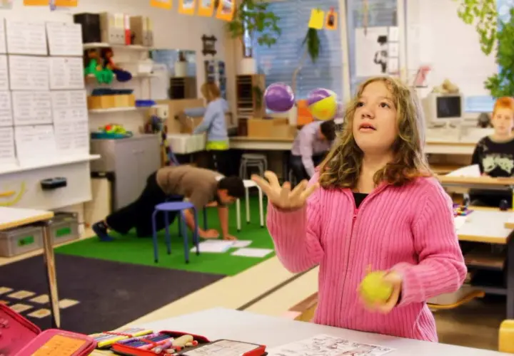 Mädchen jongliert mit Bällen im Klassenzimmer, während andere Kinder lernen. Ein Beispiel für bewegtes Lernen.