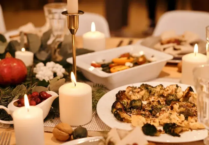 Festlich gedeckter Tisch mit Kerzenlicht, Granatapfel, Cranberry-Sauce und einem Teller mit geröstetem Gemüse – ein gesundes Weihnachtsessen.